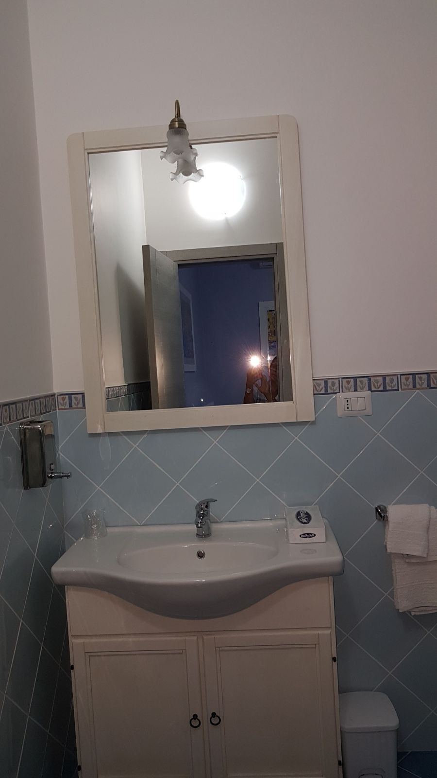 A bathroom vanity with white cabinetry, ceramic sink, and framed mirror with overhead lighting.