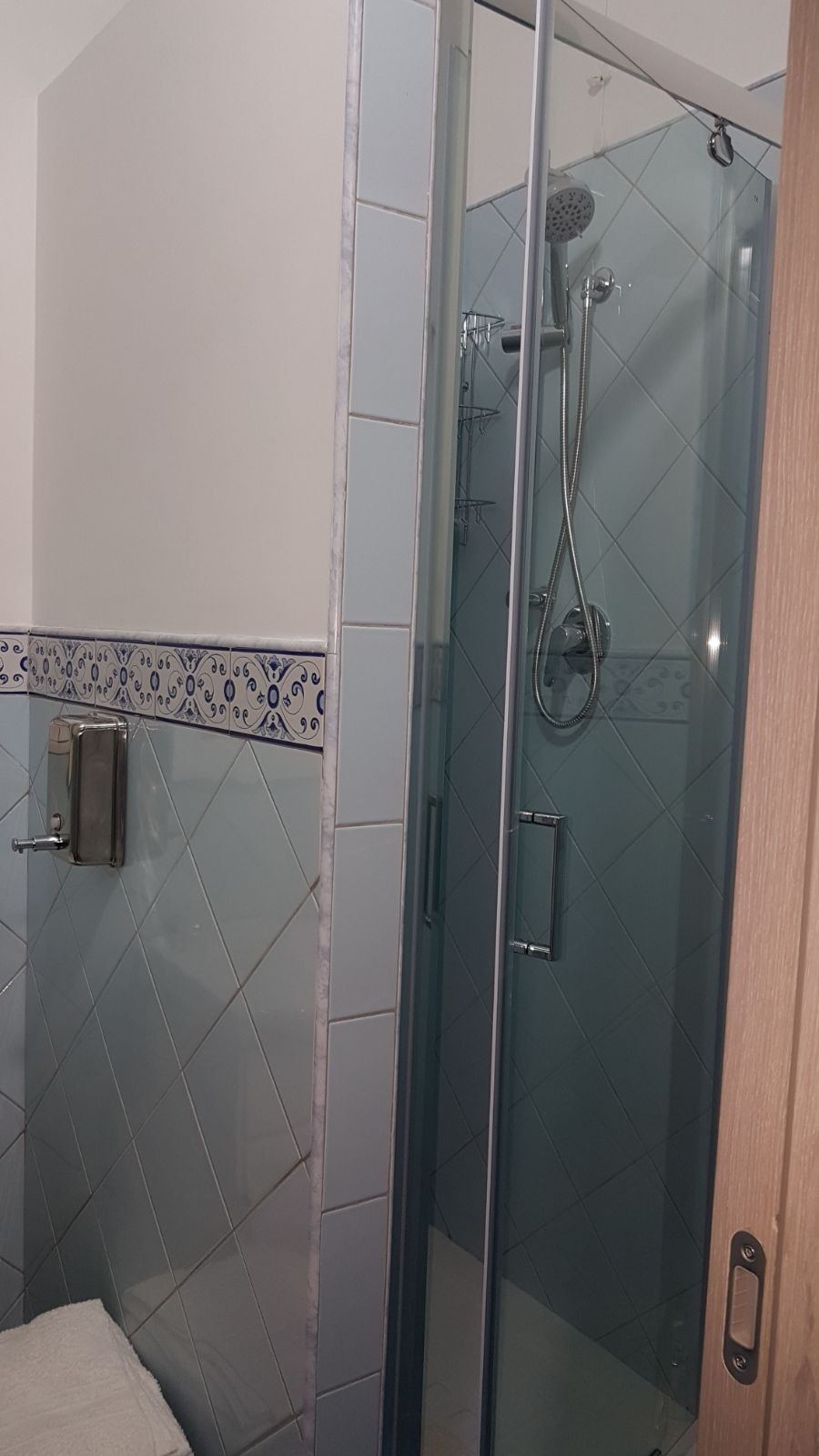 A modern bathroom shower enclosure with gray diagonal tile pattern and chrome fixtures.