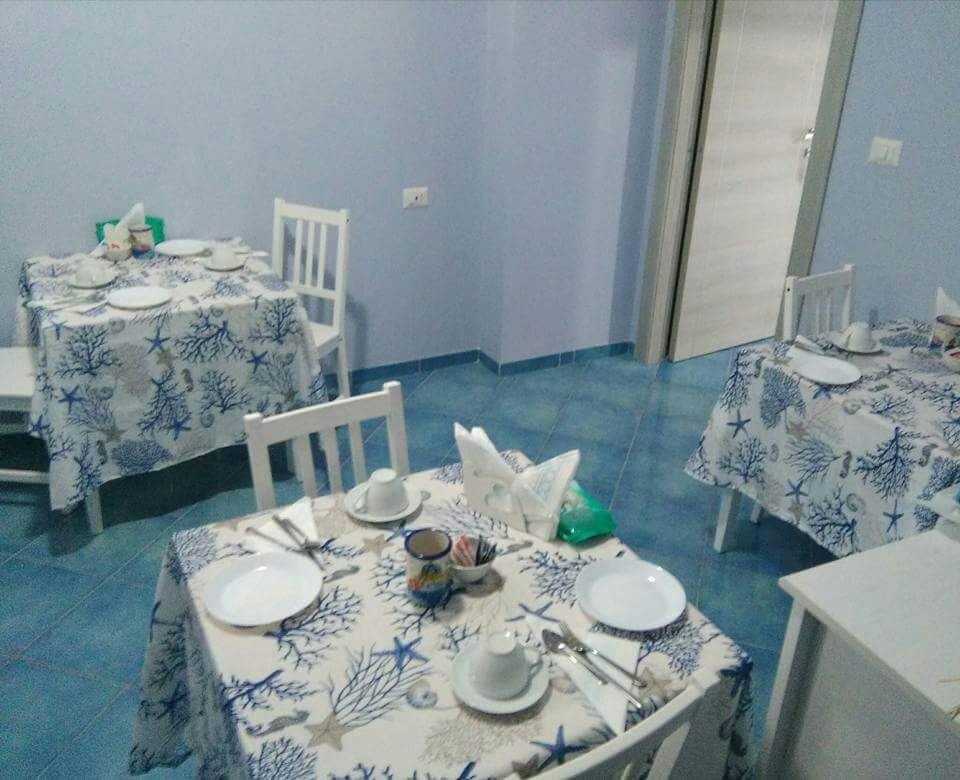 A dining room with three tables set with matching blue and white patterned tablecloths, white chairs, and place settings for guests.