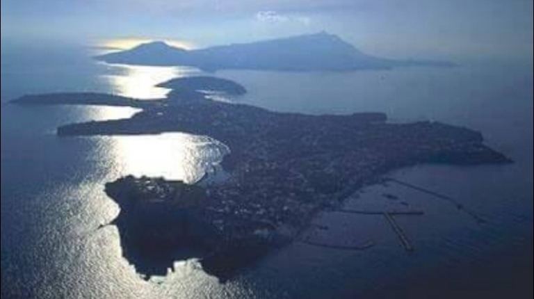 Aerial twilight view of a Mediterranean coastal town with volcanic islands and calm waters at dusk.