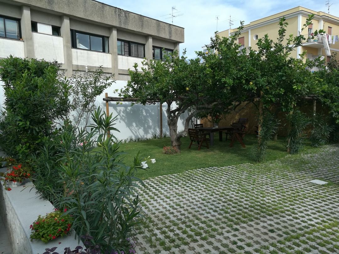 A lush garden courtyard with mature trees, pergola seating area, and manicured lawn adjacent to the bed and breakfast building.